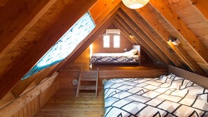 A cozy attic bedroom with a sloped ceiling, a ladder, a bed with patterned bedding, and a hanging light fixture.