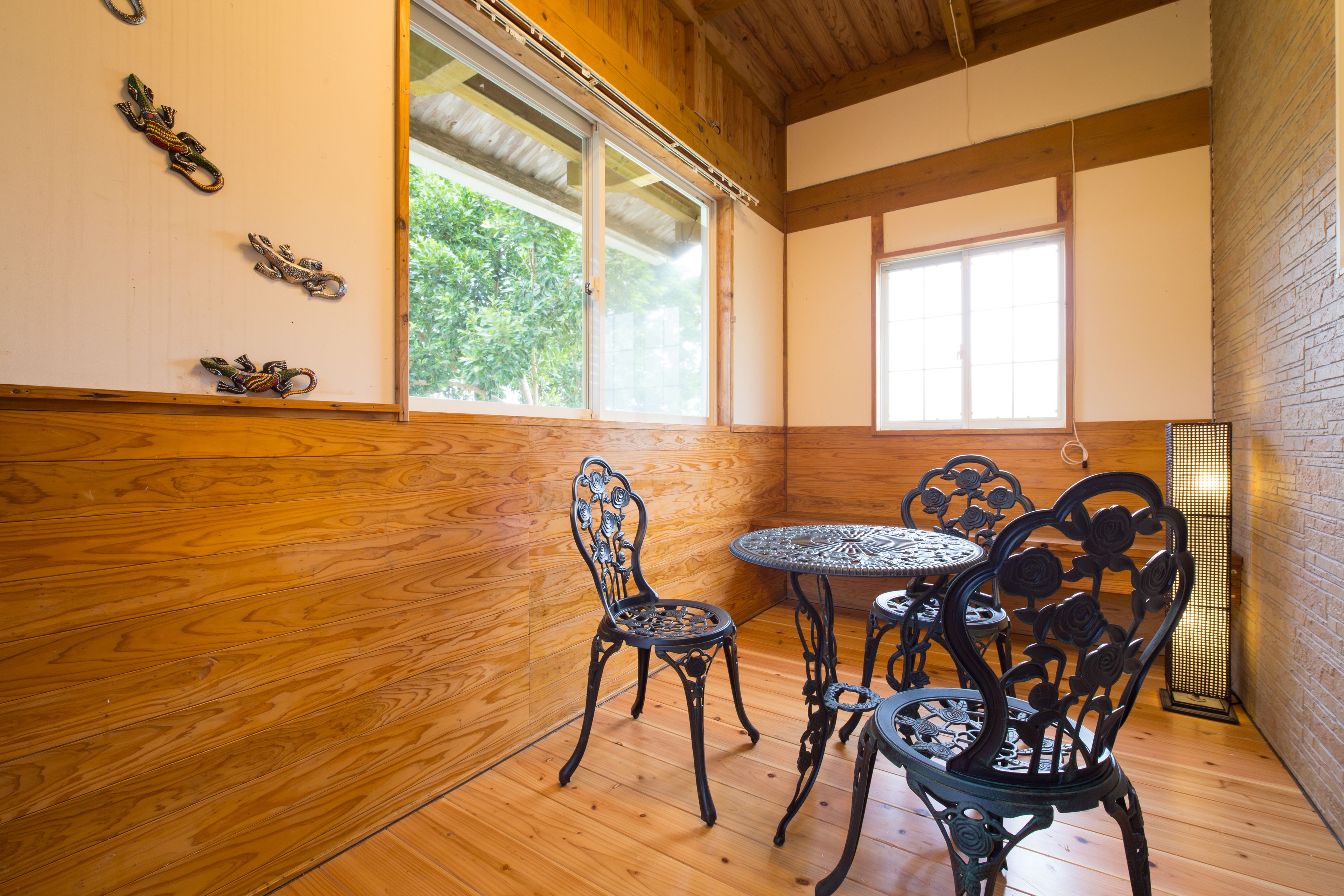 A room with wooden flooring, a round table with chairs, and a window with a view of trees.