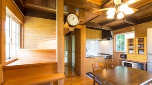 A wooden interior with a dining table, chairs, a clock, and a kitchen area.