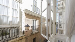 Un balcón abierto con vistas a edificios cercanos, una ventana pequeña y un farol.