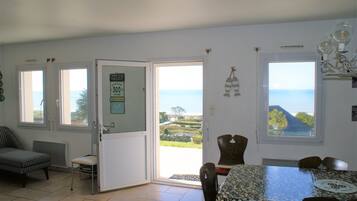Un coin repas avec une table et des chaises, une vue sur la mer par une fenêtre et une porte donnant sur l’extérieur.
