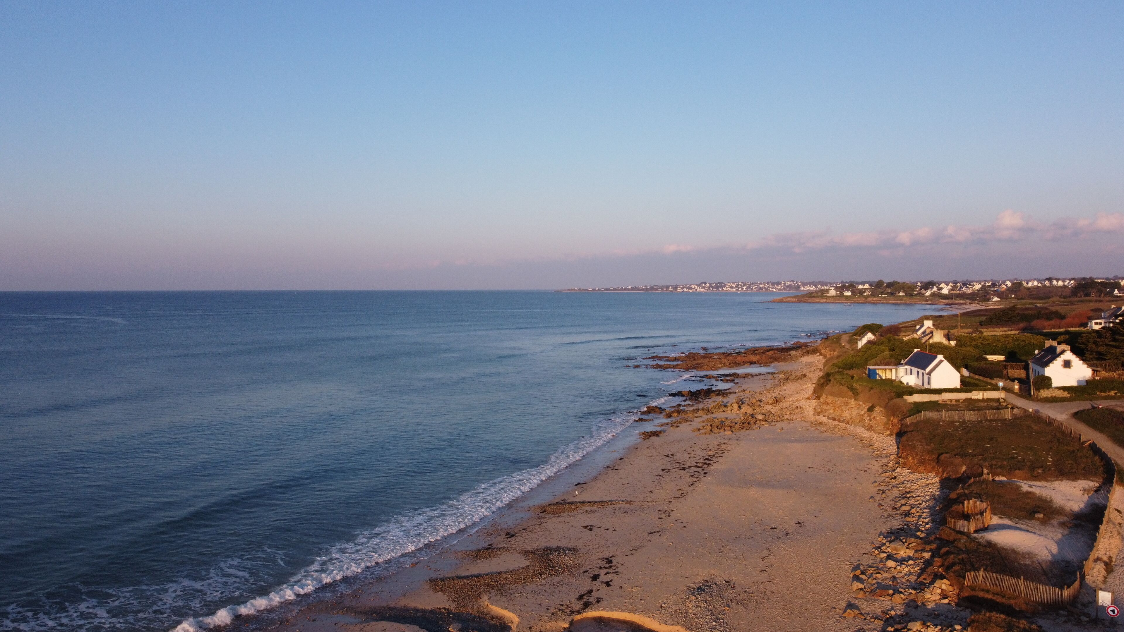 A coastal view with a sandy beach, a rocky shoreline, and white buildings along the shore.