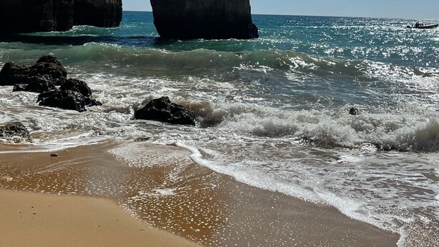 A coastal scene with a prominent rock arch formation, sandy beach, and ocean waves.