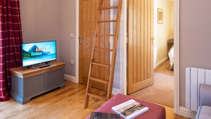 A living room with a wooden ladder, a television, and a bench with books.