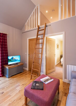 Una sala de estar con una escalera de madera, un televisor y un banco lleno de libros.