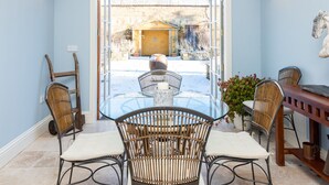 A dining area with a glass table and wicker chairs, a wooden dining table with metal chairs, and a view of a building through a glass door.