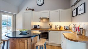 A modern kitchen with white cabinets, a round island with stools, a microwave, a toaster, and a sink.