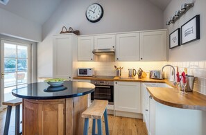 Una cocina moderna con armarios blancos, una isla redonda con taburetes, un microondas, un tostador y un lavamanos.