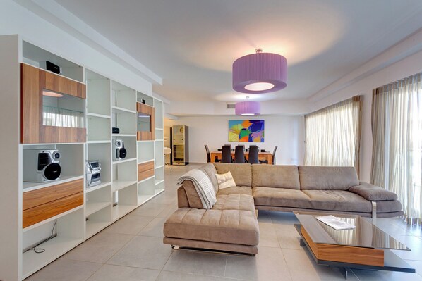 A modern living room with a sectional sofa, a coffee table, and built-in shelving with various items. - Seaview Apartment In Fort Cambridge, Sliema (Sliema)