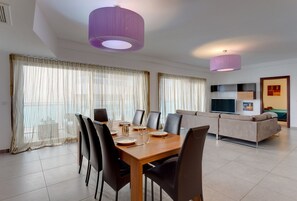 A modern dining area with a wooden table and chairs, a sofa, and a TV in the background. - Seaview Apartment In Fort Cambridge, Sliema (Sliema)