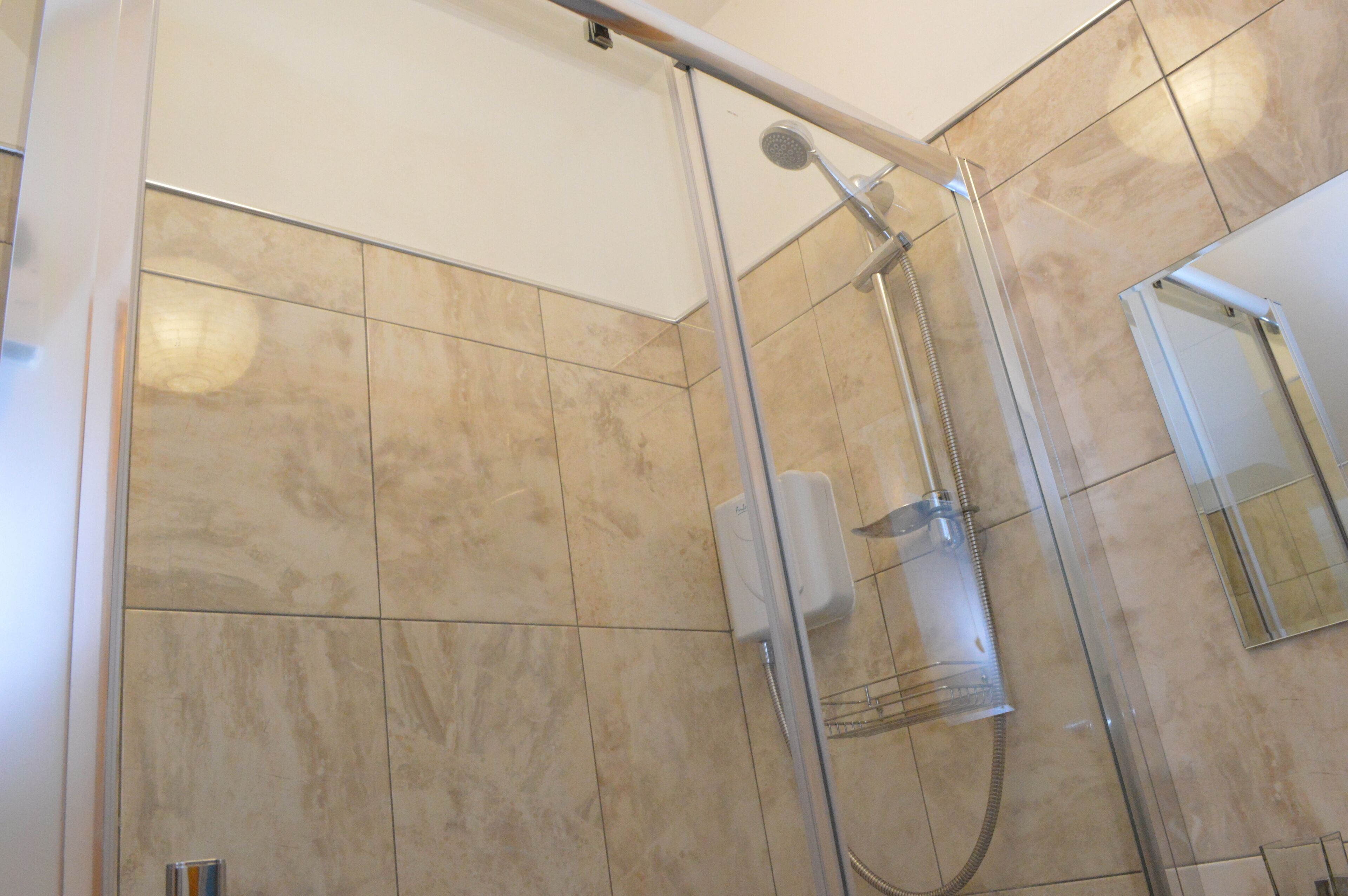 A glass-enclosed shower with a handheld showerhead and a wall-mounted control panel.