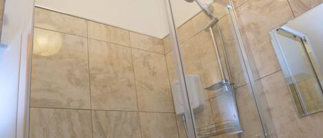 A glass-enclosed shower with a handheld showerhead and a wall-mounted control panel.