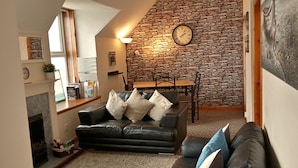 Un salon chaleureux avec un mur en pierre, une cheminée, un canapé en cuir noir et une table à manger avec des chaises.