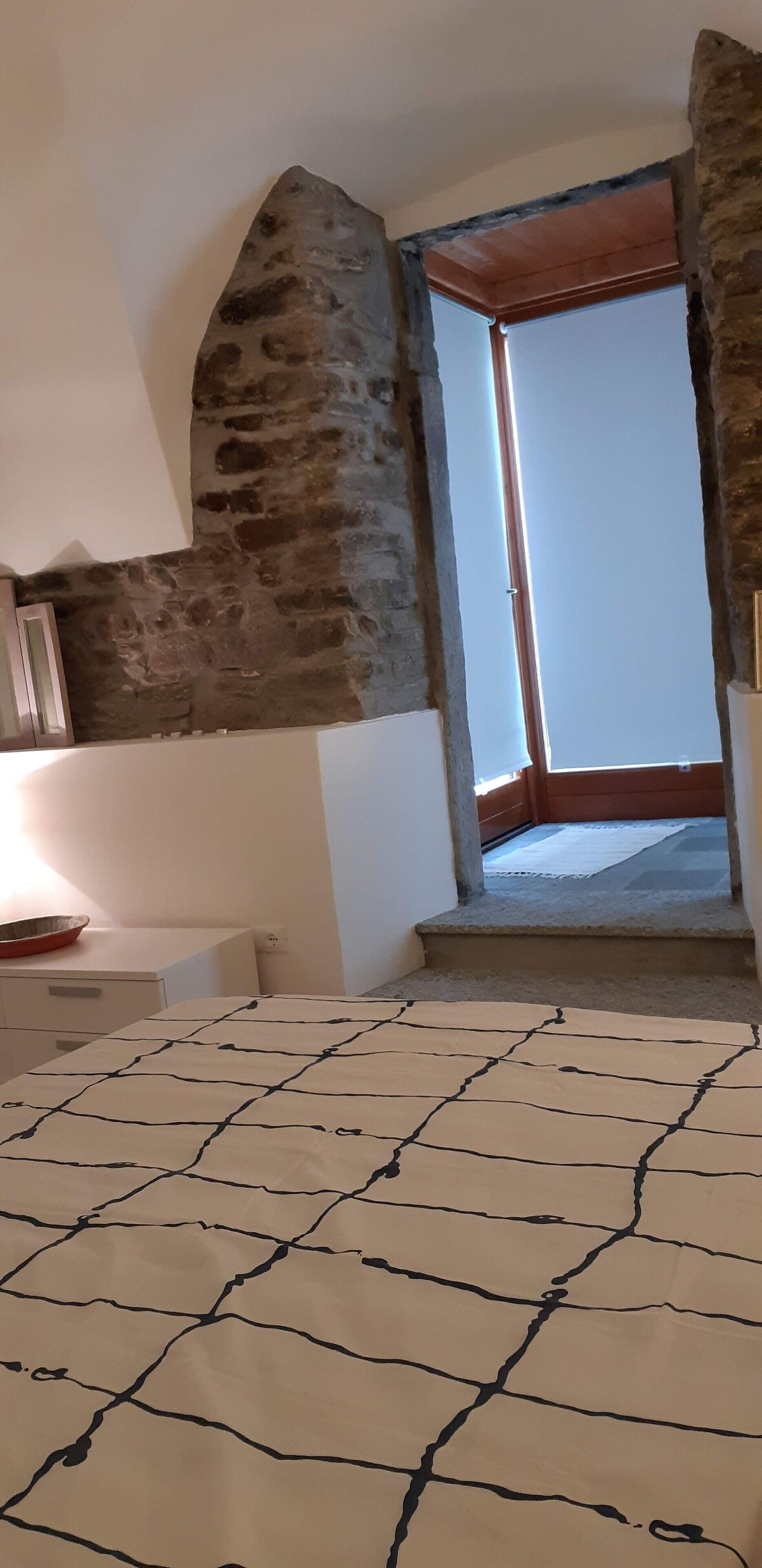 Une pièce avec un mur en pierre, une porte blanche et une couvre-lit à motifs.