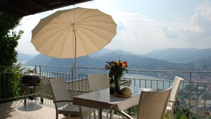A terrace with a table, chairs, an umbrella, and a view of mountains and a lake. - Nice apartment in villa with WIFI, private pool, TV, terrace, pets allowed and panoramic view (Lugano)