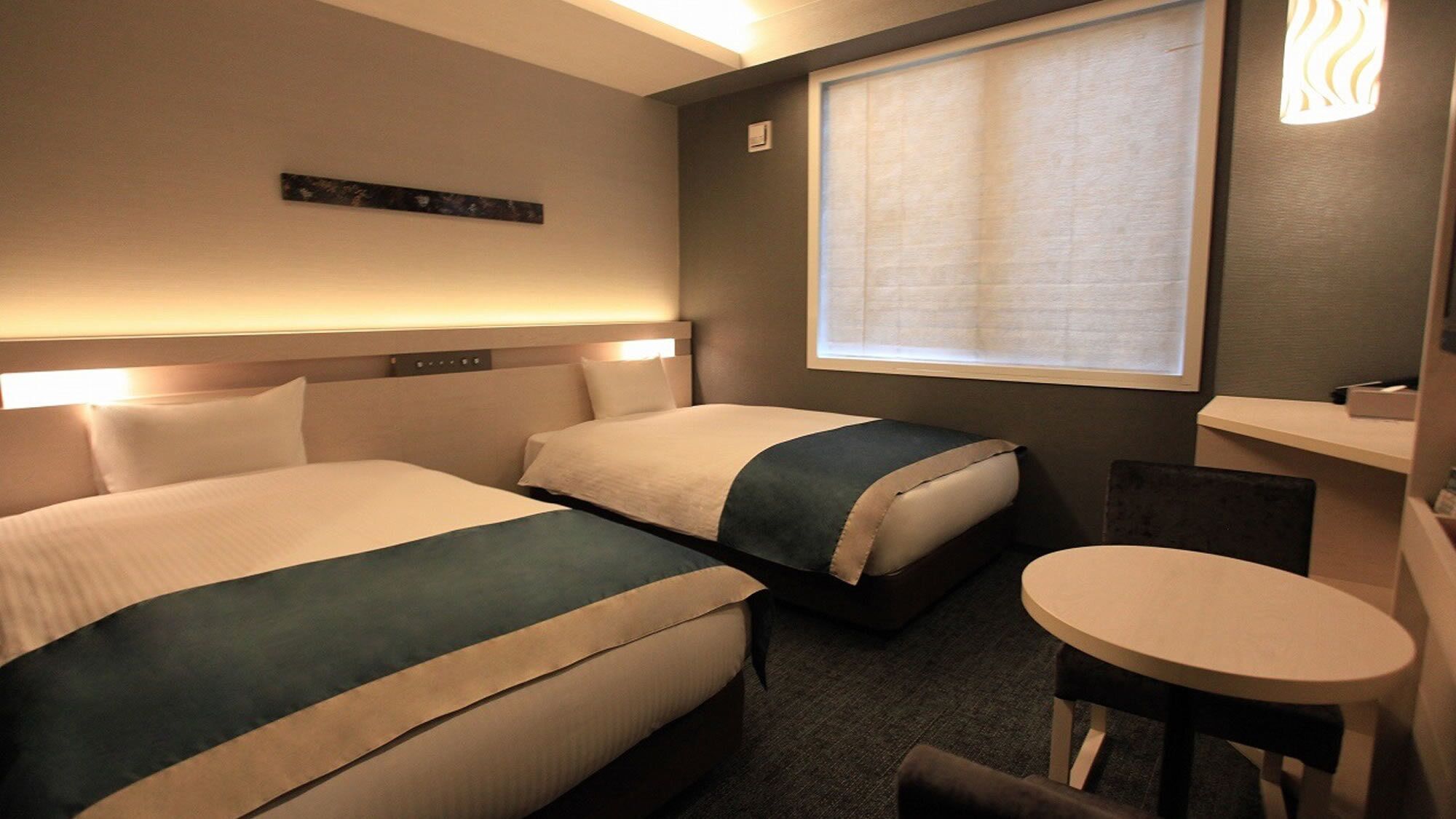 Habitación de hotel con dos camas, una mesita y una ventana con persianas.