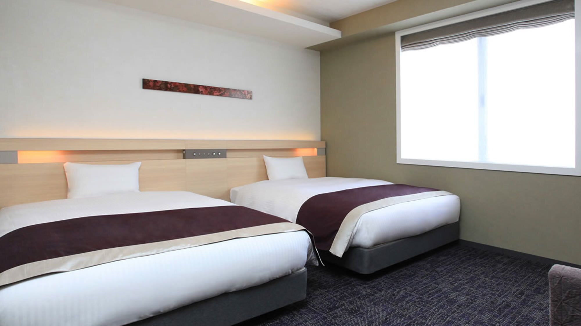 Quarto de hotel com duas camas, janela com persianas, cabeceira com painel de luz e uma pequena obra de arte na parede.