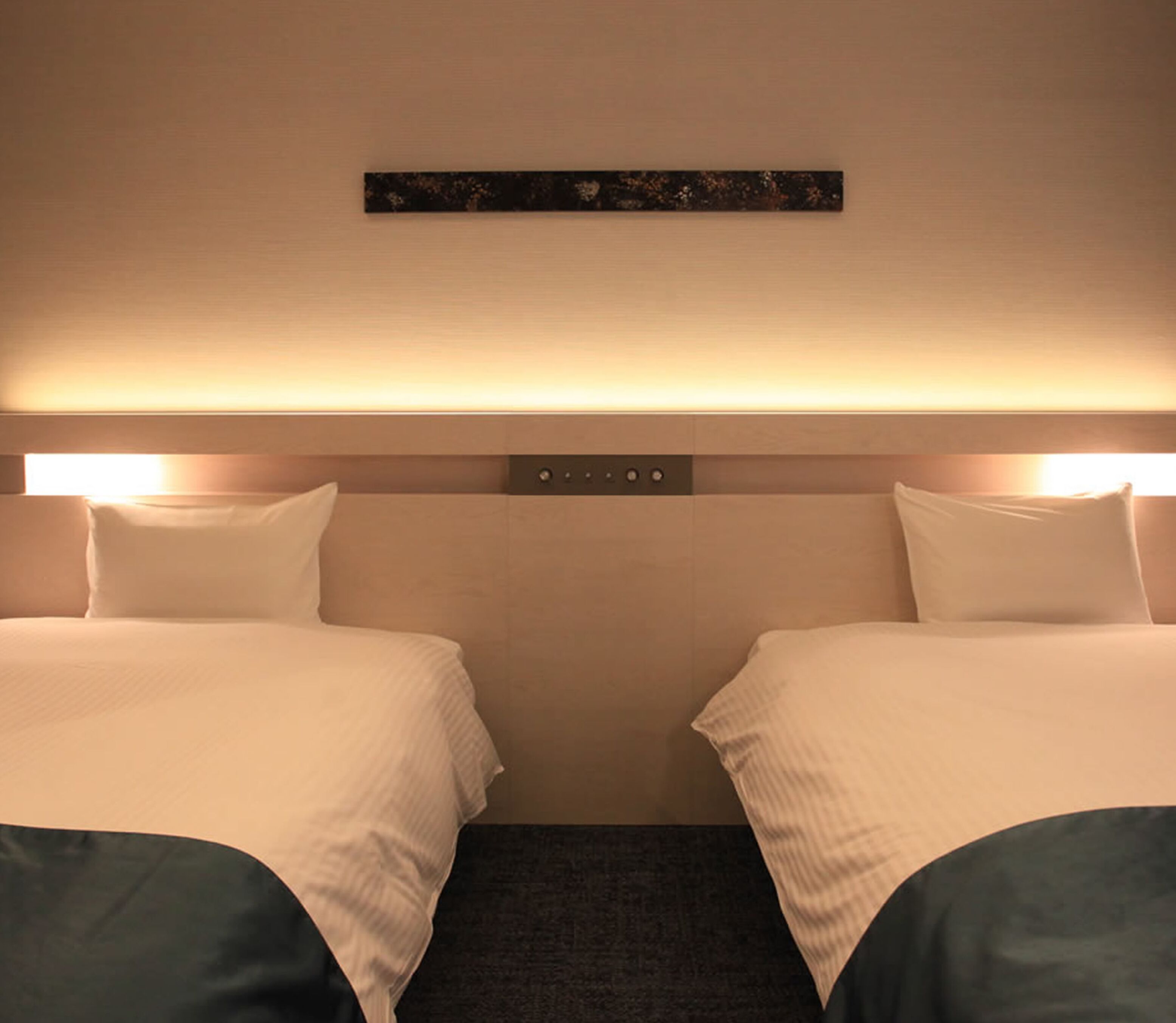Une chambre d’hôtel avec deux lits, une tête de lit dotée de commandes et une petite œuvre d’art au-dessus des lits.