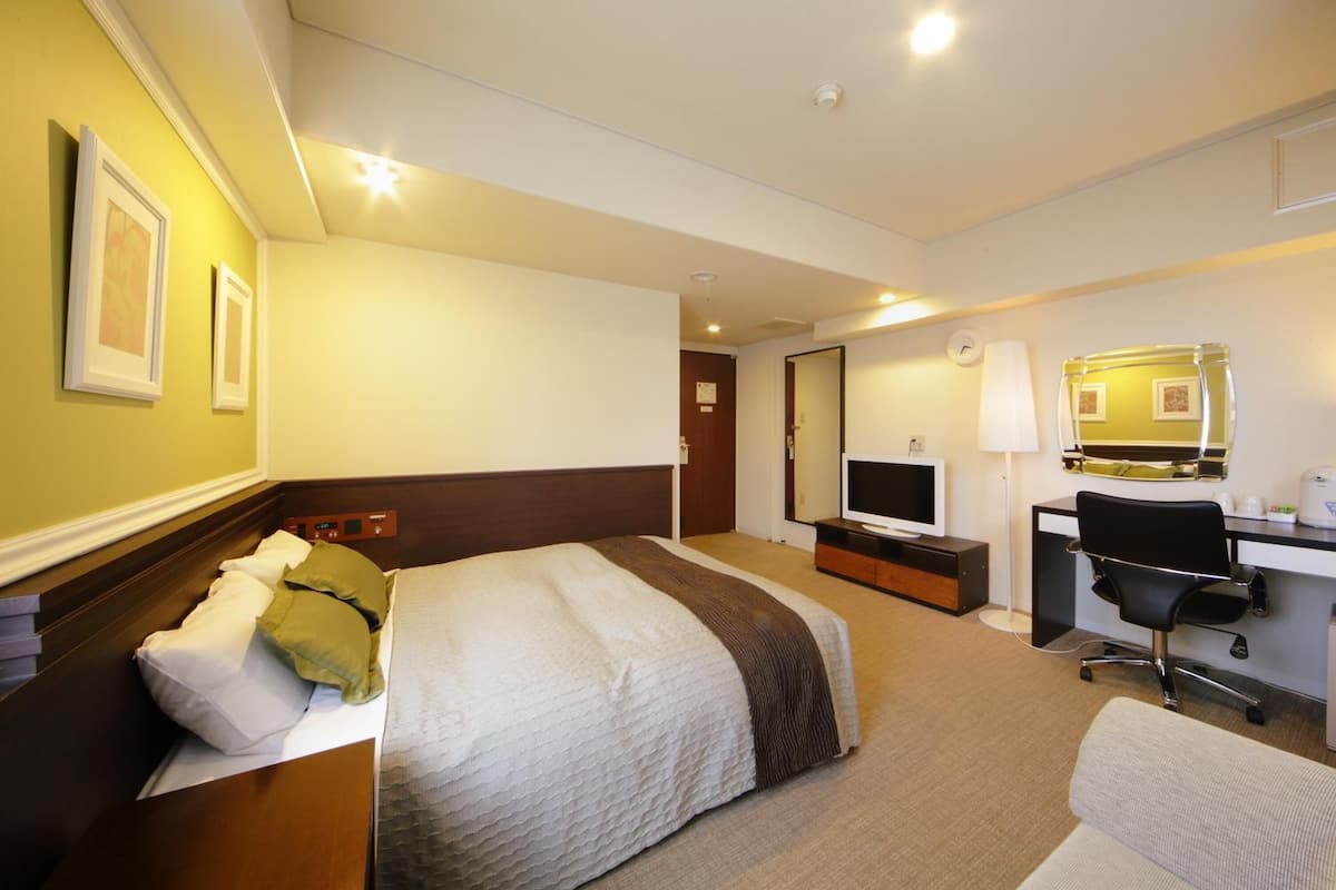 Ein Hotelzimmer mit Bett, Schreibtisch, Computer, Fernseher und Spiegel.