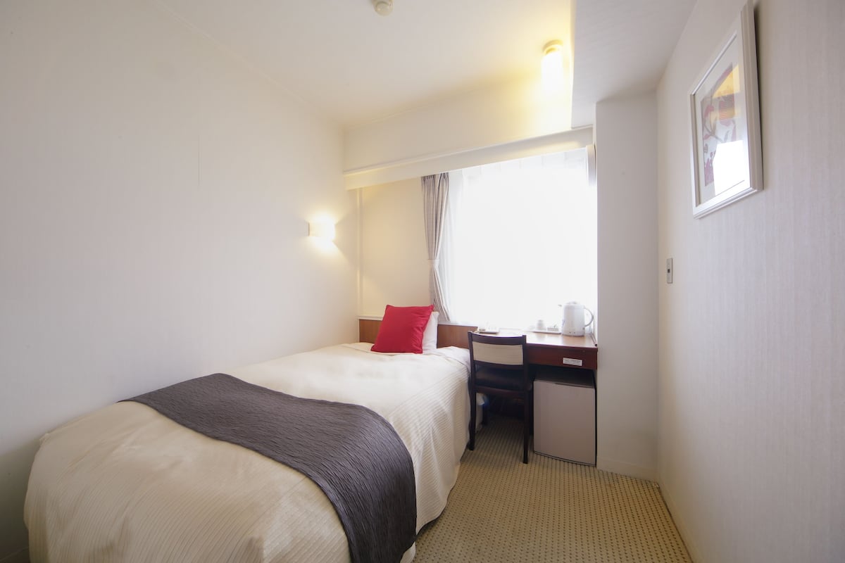 Ein Hotelzimmer mit Bett, Schreibtisch, Stuhl und einem Vorhangfenster.