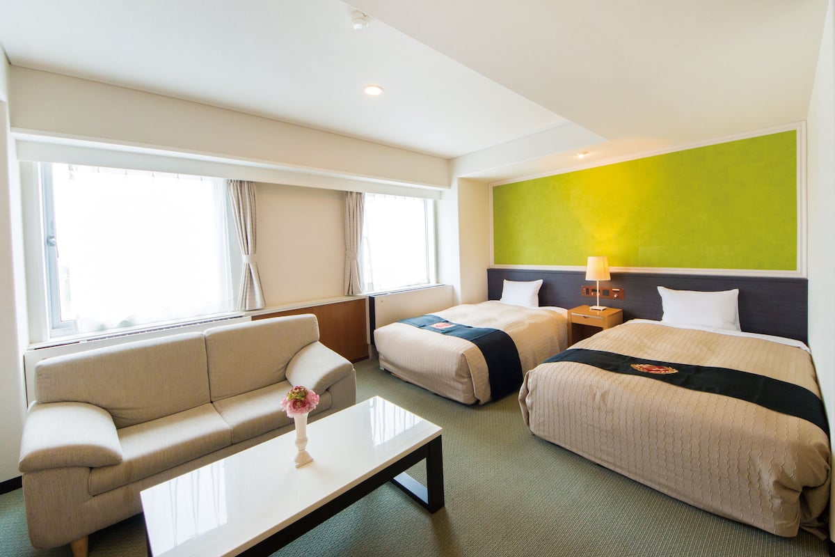 Ein Hotelzimmer mit einer Couch, einem Bett, einem Nachttisch und einem Fenster mit Vorhängen.