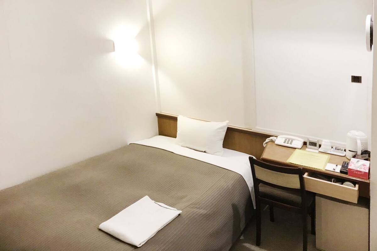 Ein Hotelzimmer mit einem Einzelbett, einem Schreibtisch mit Telefon und einem kleinen Schrank.