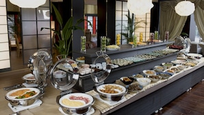 Ein reichhaltiges Buffet mit verschiedenen Speisen in einem modernen Innenraum mit großen Fenstern und Vorhängen.