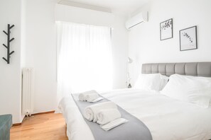 Un llit ben arropat amb llençols blancs i tovalloles esteses, un capçal gris i un radiador a la paret.