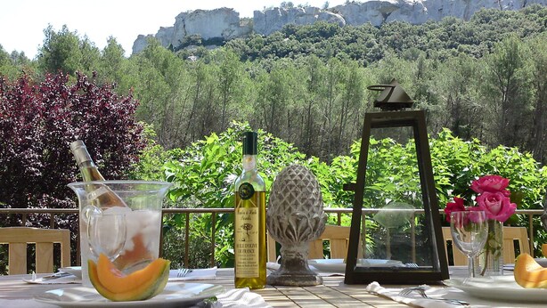 A table set outdoors with a bottle of wine, a glass with a melon slice, a decorative vase, and a framed picture. - Magnificent Bastide in the heart of alpilles, quiet absolute, exceptional position, private Tennis, Swimming pool warmed 7 rooms 4 bathrooms (Fontvieille)