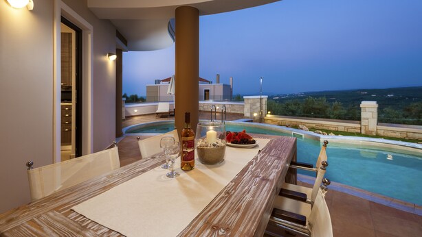 A dining area with a pool view, a bottle of wine, and a candle on the table. - Villa Stellina, elegant villa, full privacy (Chania)