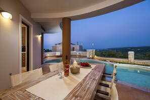 A dining area with a pool view, a bottle of wine, and a candle on the table. - Villa Stellina, elegant villa, full privacy (Chania)