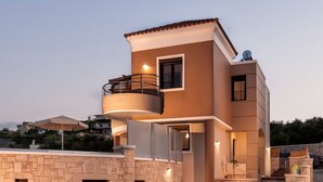 A modern two-story house with a stone facade, a balcony, and a well-lit entrance. - Villa Stellina, elegant villa, full privacy (Chania)