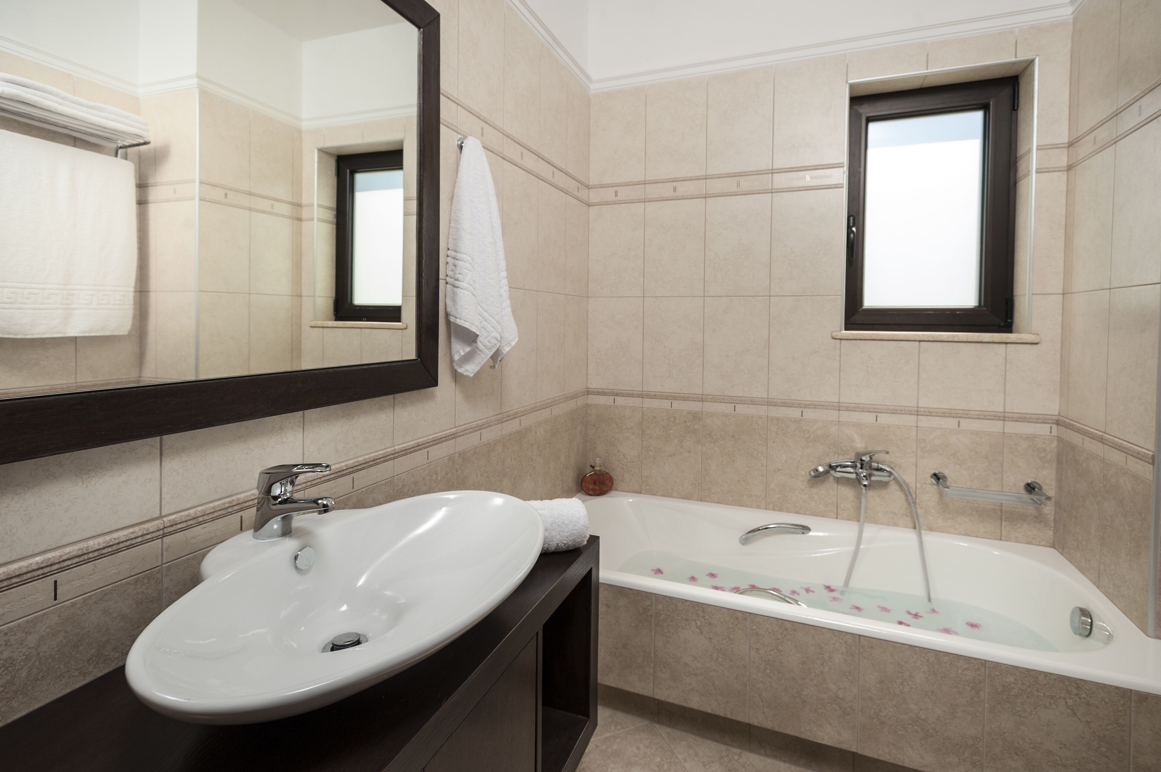 Ein Badezimmer mit einem weißen Waschbecken, einer Badewanne, einem Spiegel und einem Fenster.