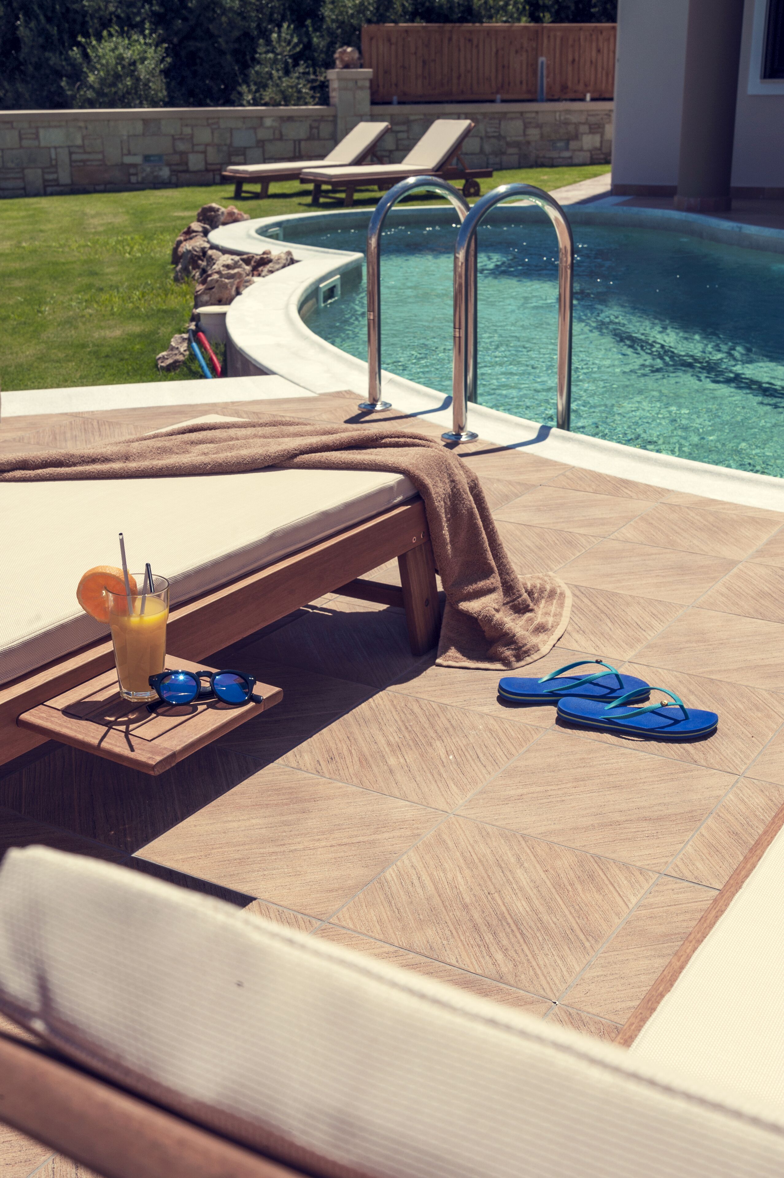 Ein Poolbereich mit Liegestühlen, einem Pool und einem Getränk mit Sonnenbrille auf einem Tablett.