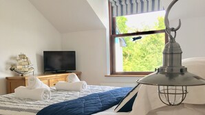 A bedroom with a bed, a bedside table, a lamp, a TV, and a window with curtains.