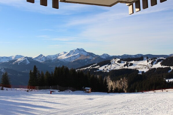 A snowy mountain landscape with a ski resort in the foreground, featuring ski slopes and a small cabin.
