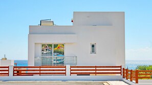 A modern building with a balcony, a view of the sea, and a red fence.