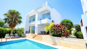 Uma casa moderna de dois andares, com piscina, área de estar externa e vegetação exuberante.