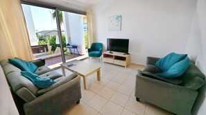 Uma sala de estar moderna com dois sofás, uma mesa de centro, uma TV e um piano ao fundo.