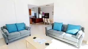 A living room with two grey sofas, a coffee table, and a kitchen in the background.