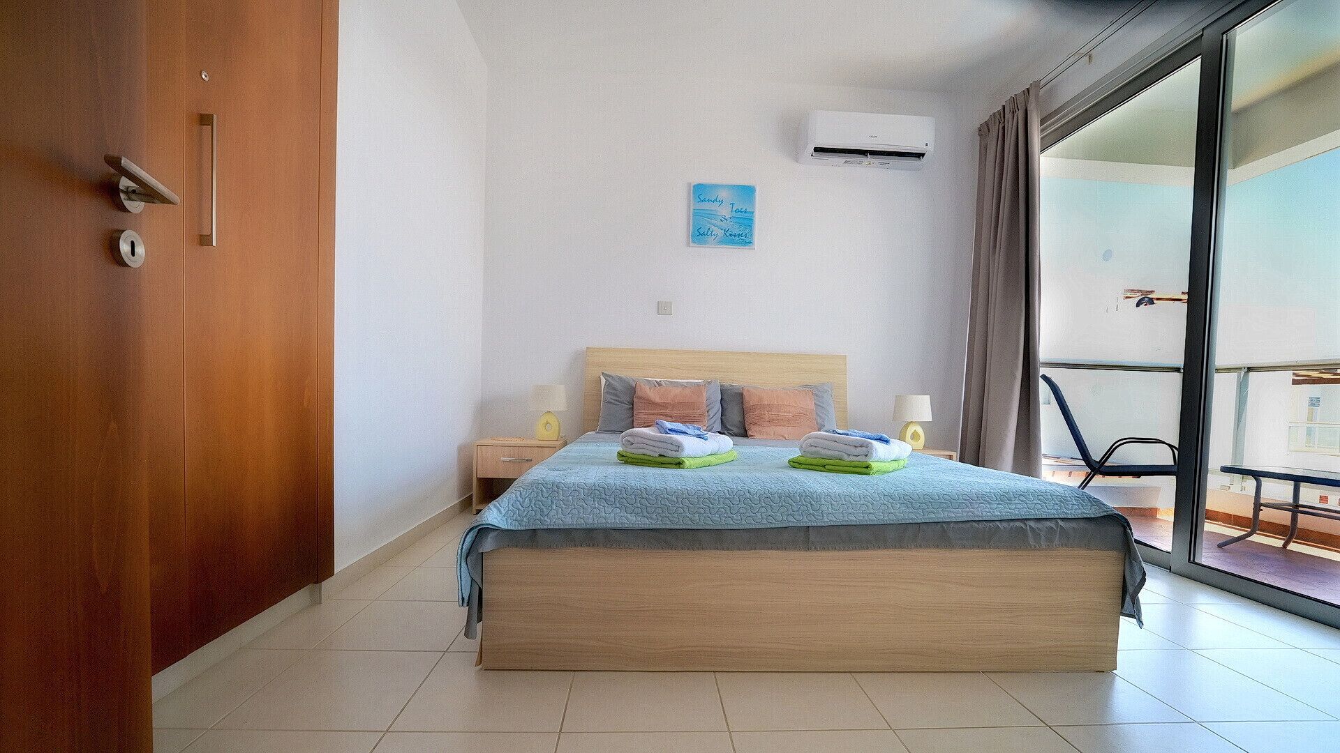 A hotel room with a bed, a nightstand, a wall-mounted air conditioner, and a view through a sliding glass door.