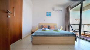 A hotel room with a bed, a nightstand, a wall-mounted air conditioner, and a view through a sliding glass door.