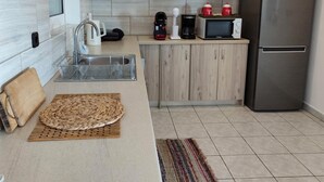 Una cocina moderna con un refrigerador de acero inoxidable, un microondas, una cafetera y un hervidor en la encimera. Hay un felpudo tejido en la encimera y una alfombra a rayas en el suelo.