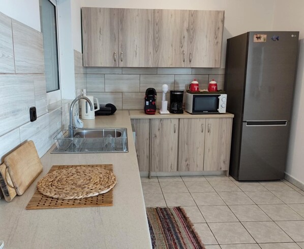 Una cocina moderna con un refrigerador de acero inoxidable, un microondas, una cafetera y un hervidor en la encimera. Hay un felpudo tejido en la encimera y una alfombra a rayas en el suelo.
