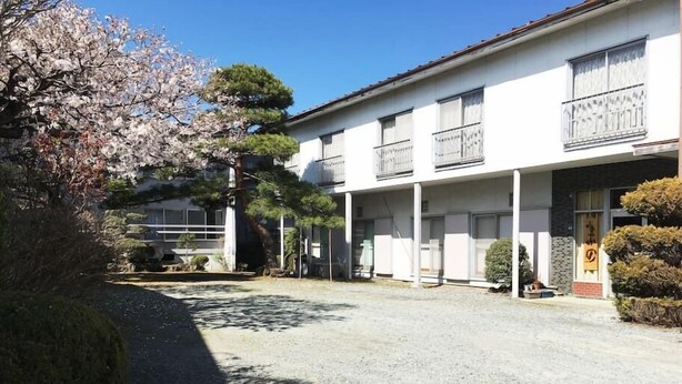 A building with a covered entrance, a parking area, and a cherry blossom tree. - Nakano (Fujiyoshida)