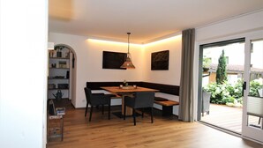 Een eetgedeelte met een houten tafel, vier stoelen, een bank en een hanglamp.