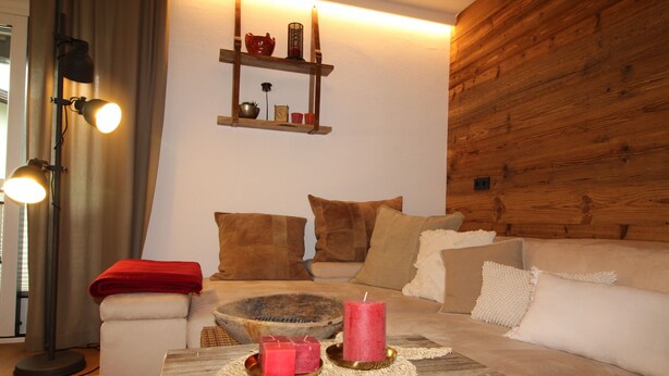Een gezellige woonkamer met een bank, een bijzettafeltje met kaarsen, een vloerlamp en een houten wand.