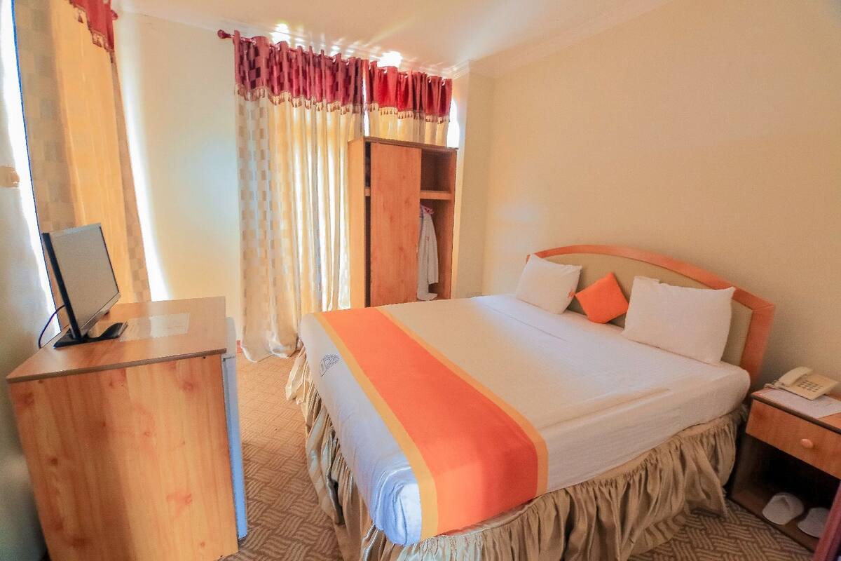 Une chambre d’hôtel comprenant un lit, un bureau avec un ordinateur, une armoire et un téléphone.