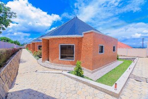 Uma casa de tijolos com telhado azul, um caminho de paralelepípedos e uma pequena área ajardinada.