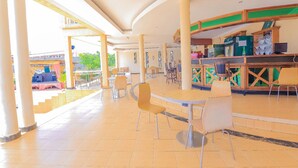 Um espaço amplo e coberto, com várias mesas e cadeiras, um balcão com diversos itens e vista para o exterior.